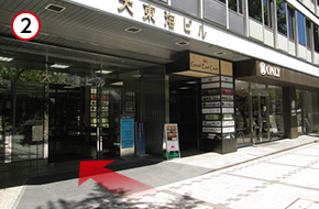 12番出口を出ると、すぐ左手にセブンイレブンが入っているビルが見えます。このビルです。大東海ビルの2階へお越しください。セブンイレブン、ONLYの間がビルの入り口です。